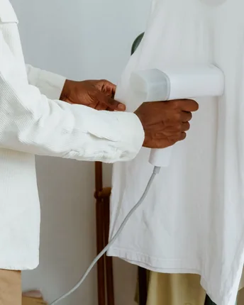 A handheld garment steamer being run down a white shirt on a rail.